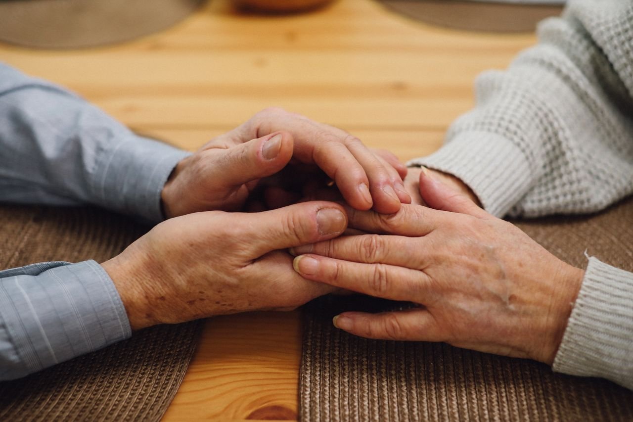 An older couple holding hands across a wooden kitchen table