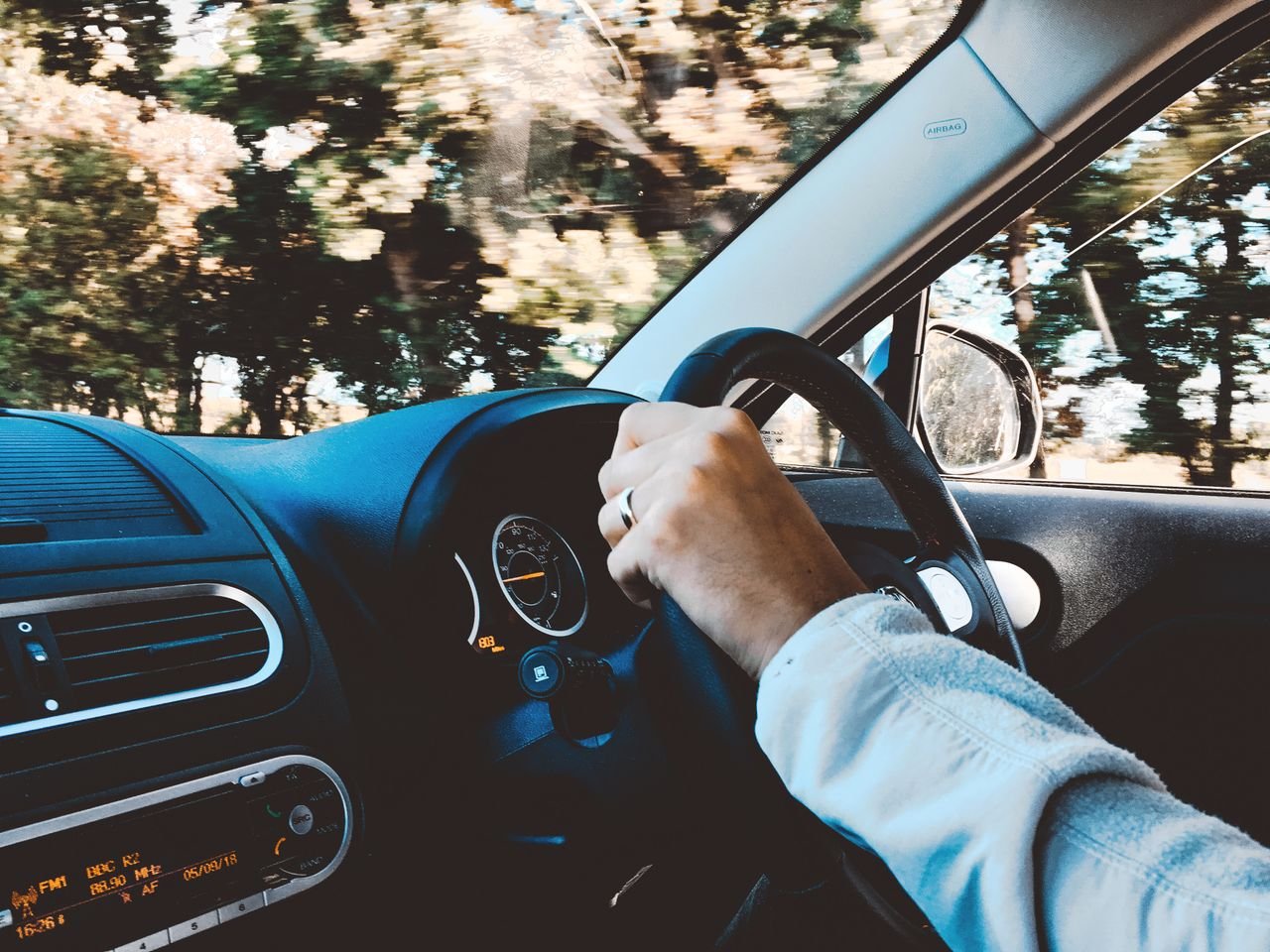 A driver’s hand on the steering wheel of a car on a sunny road