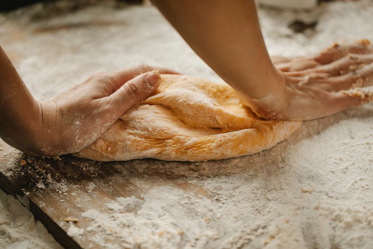 A baker’s hands kneading dough on a floured wooden table