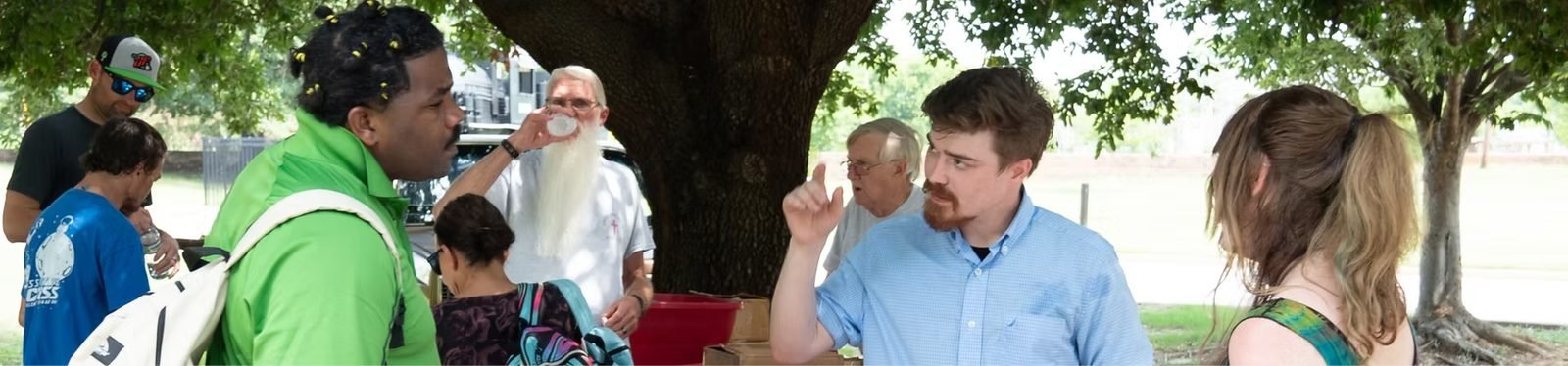 Neighbors gathered and talking under the trees at a Life and Health For All community outreach event