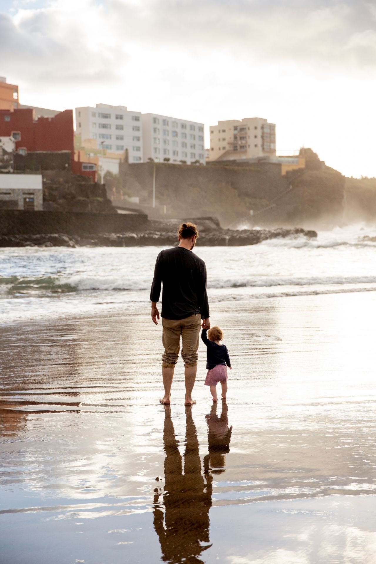 A parent and a small child walking along the shore at the water’s edge
