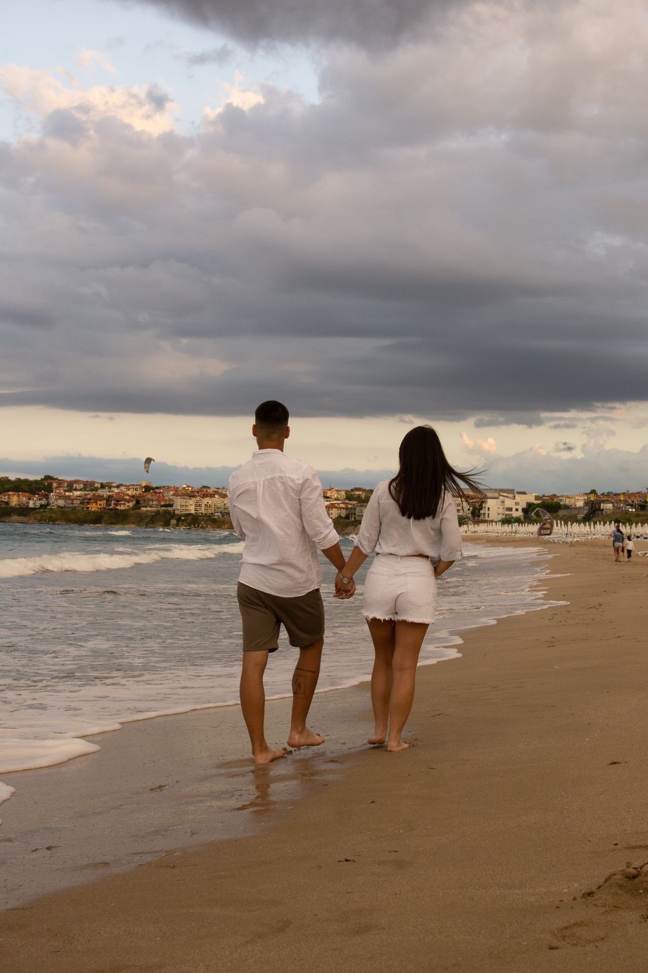 A couple walking hand in hand along the beach under a cloudy sky