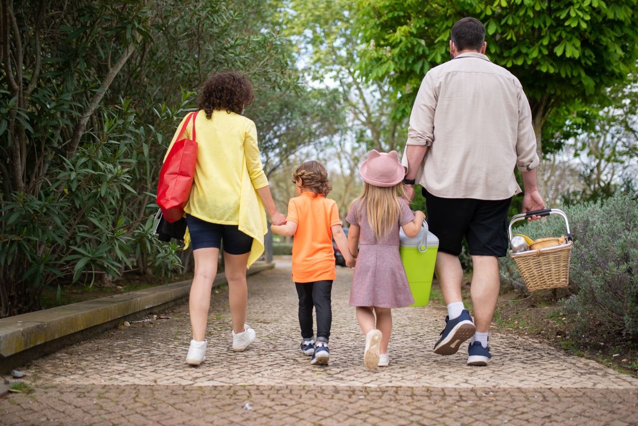 Parents and their two children walking together through a park, seen from behind