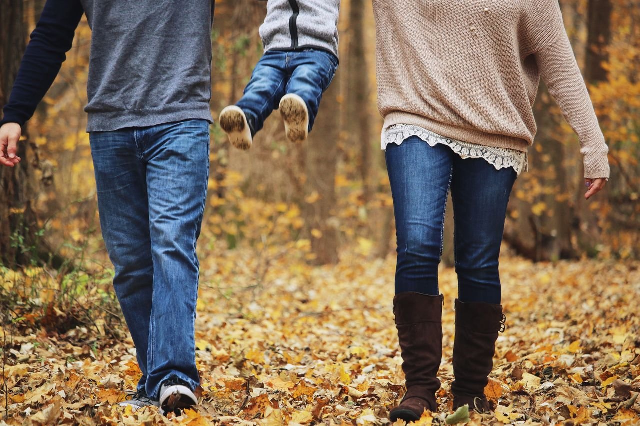 Parents swinging their child between them on an autumn walk through fallen leaves